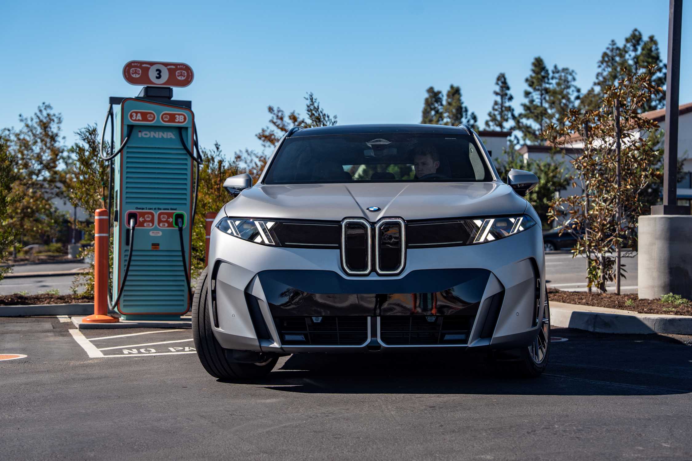 Silberner BMW iX5 60 xDrive neben einer türkisfarbenen IONNA-Schnellladesäule