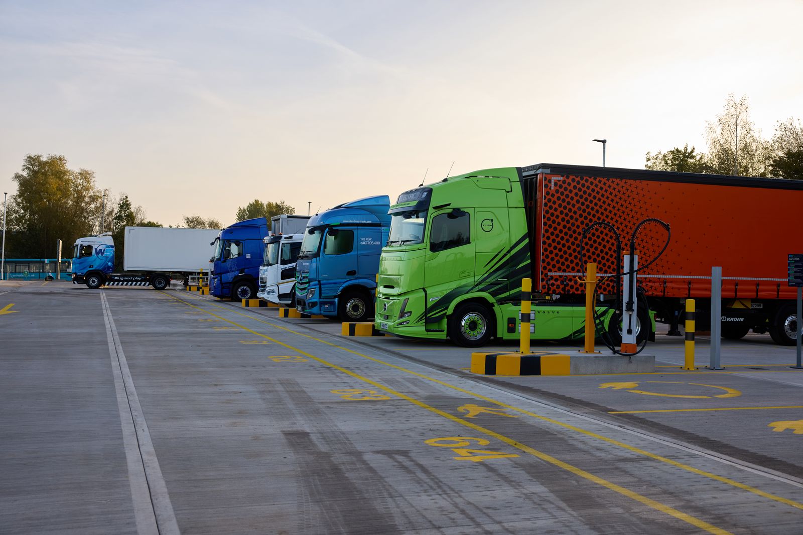 Grüne Zugmaschine und weitere Lkw neben einer Ladesäule im Electroway-Ladepark in Lutterworth
